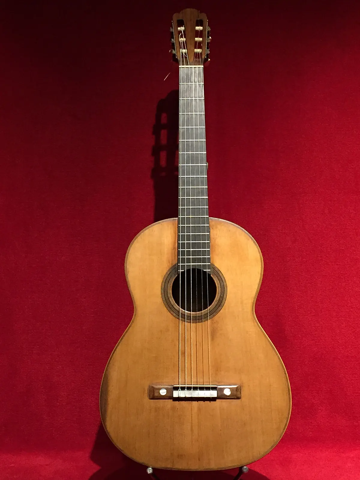 A 19th-century Spanish guitar with a pale spruce top, a rosette around the sound hole and a bridge with tie block, on a red cloth background